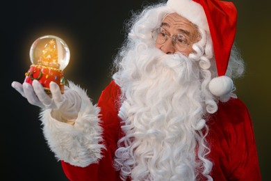 Photo of Merry Christmas. Santa Claus with snow globe on dark background