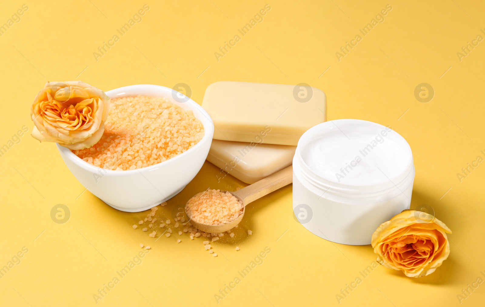 Photo of Sea salt, soap bars, jar of cream and beautiful roses on yellow background