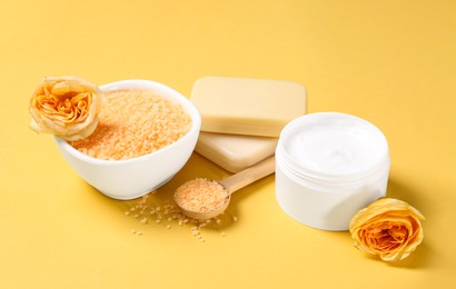 Sea salt, soap bars, jar of cream and beautiful roses on yellow background