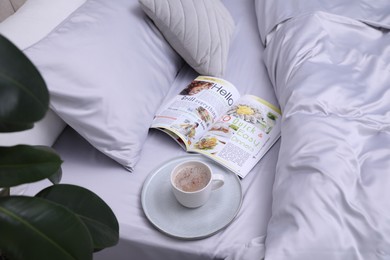 Photo of Cup of coffee and magazine on bed with soft silky bedclothes