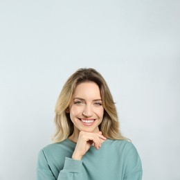 Portrait of happy young woman with beautiful blonde hair and charming smile on light background