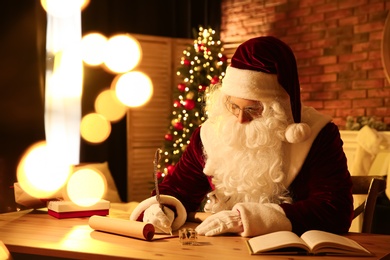 Photo of Santa Claus writing letter at table indoors