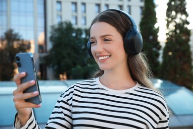 Photo of Smiling woman in headphones using smartphone on city street