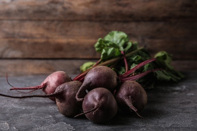 Photo of Bunch of fresh beets with leaves on grey table against wooden background. Space for text