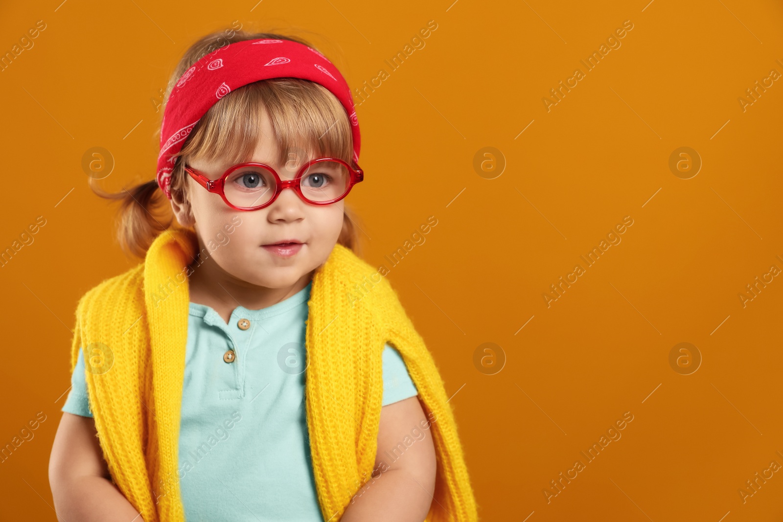 Photo of Cute little girl in glasses on orange background. Space for text