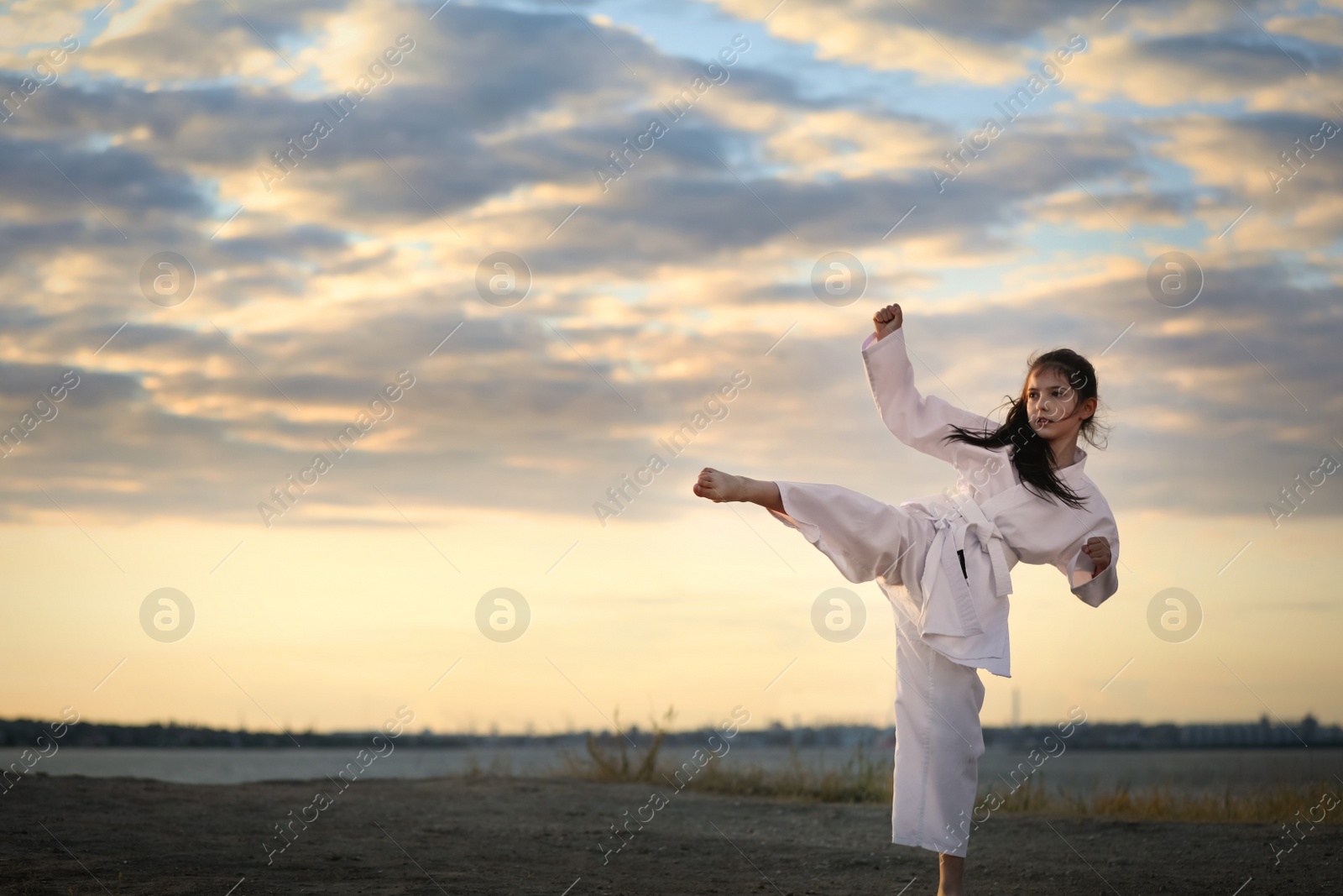 Photo of Cute little girl in kimono practicing karate outdoors