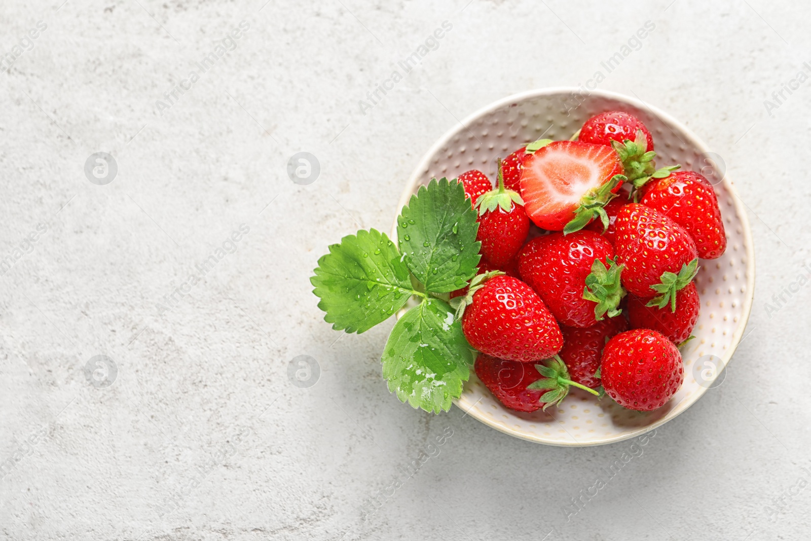 Photo of Bowl with ripe strawberries on light background, top view