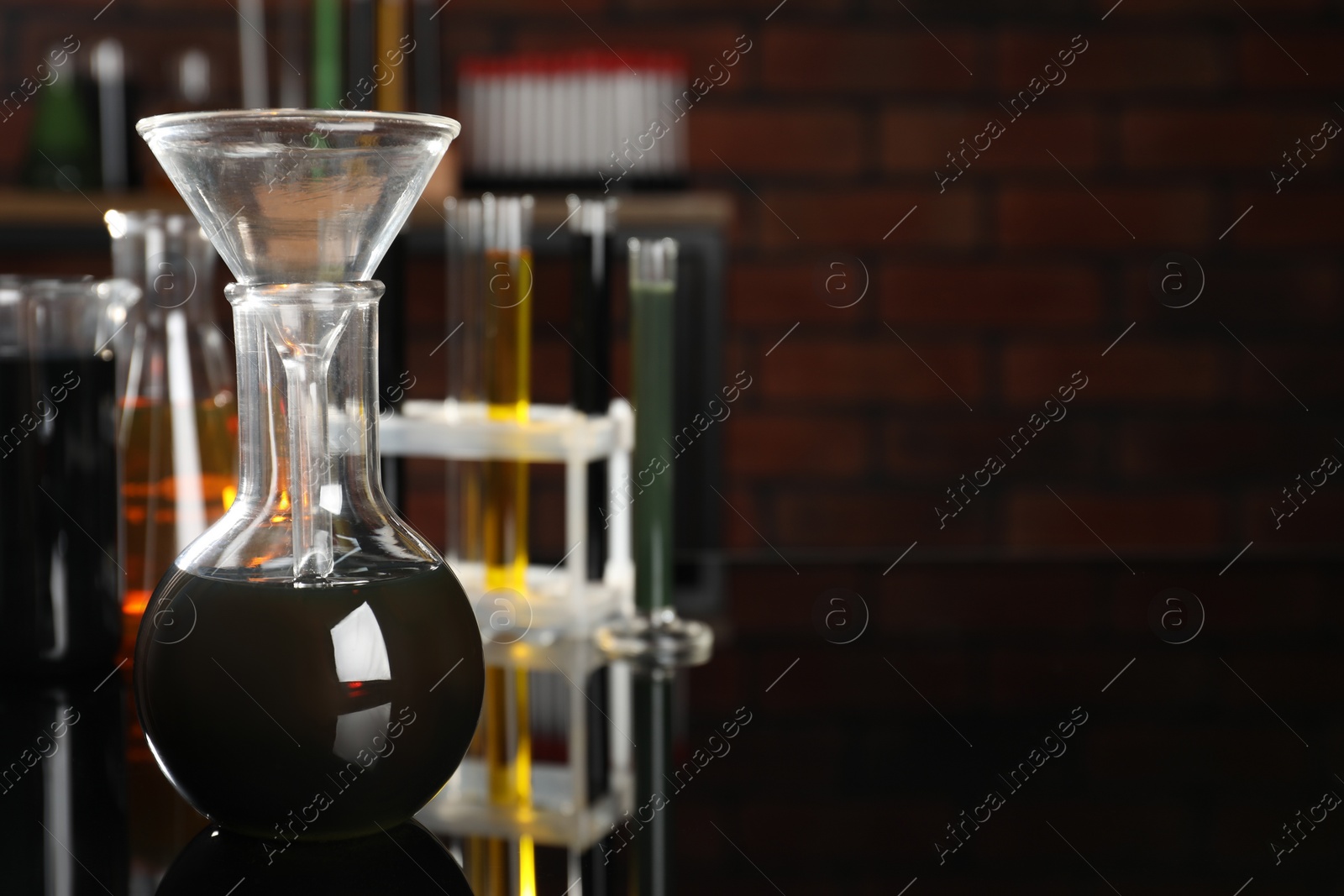 Photo of Laboratory glassware with different types of oil on black mirror table indoors, closeup. Space for text