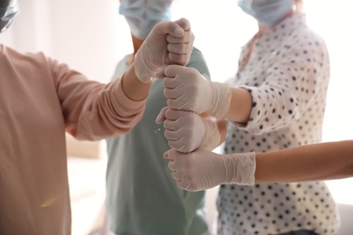 People in white medical gloves stacking fists on light background, closeup