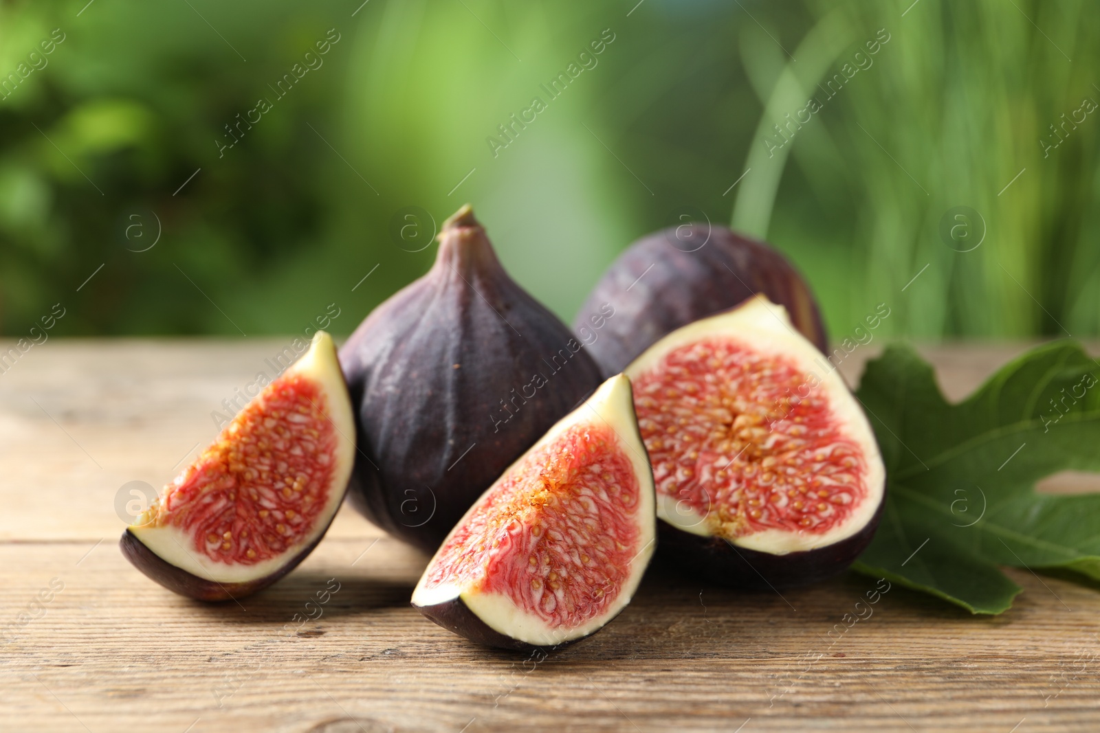 Photo of Fresh ripe figs and green leaf on wooden table, closeup