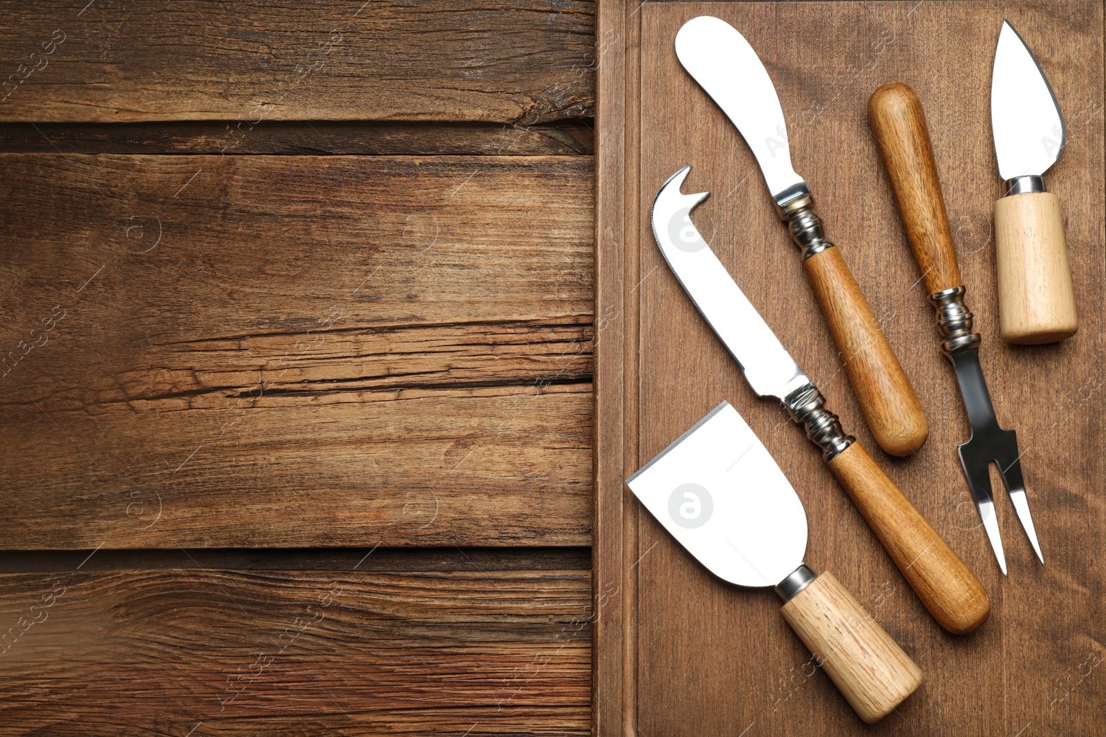 Photo of Cheese knives and fork on wooden table, flat lay. Space for text