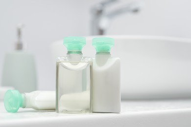 Mini bottles of cosmetic products on white countertop in bathroom. Space for text