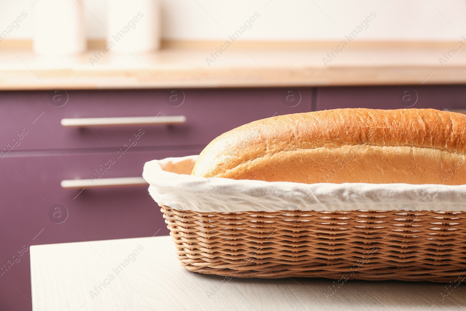 Photo of Wicker basket with loaf of tasty fresh bread on wooden table in kitchen