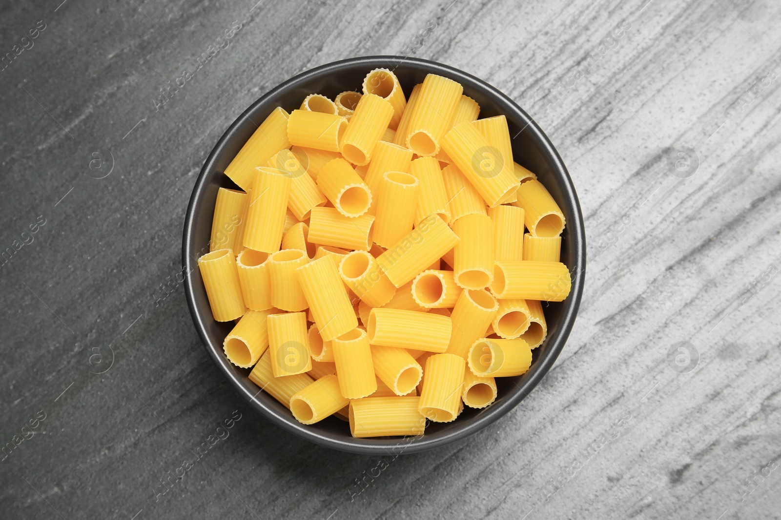 Photo of Raw rigatoni pasta in bowl on grey table, top view