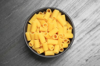 Raw rigatoni pasta in bowl on grey table, top view