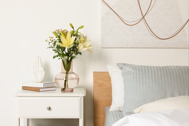 Vase with bouquet of fresh flowers on white nightstand in bedroom