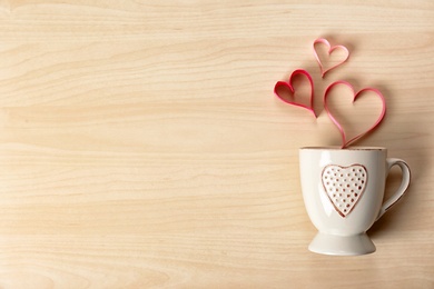 Photo of Cup and hearts made of ribbons on wooden background, top view with space for text