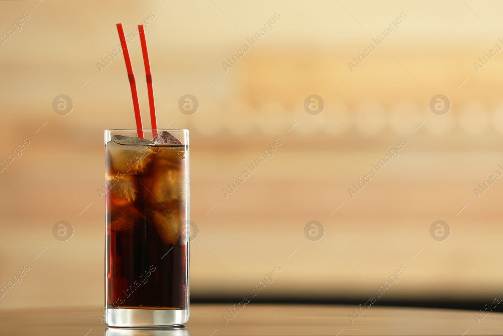 Photo of Glass of cola with ice on table against blurred background. Space for text