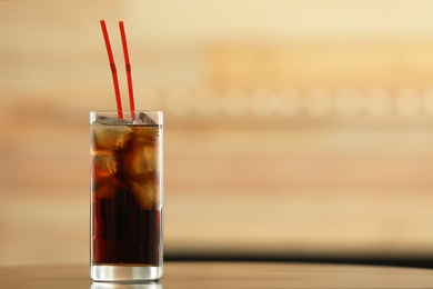 Glass of cola with ice on table against blurred background. Space for text