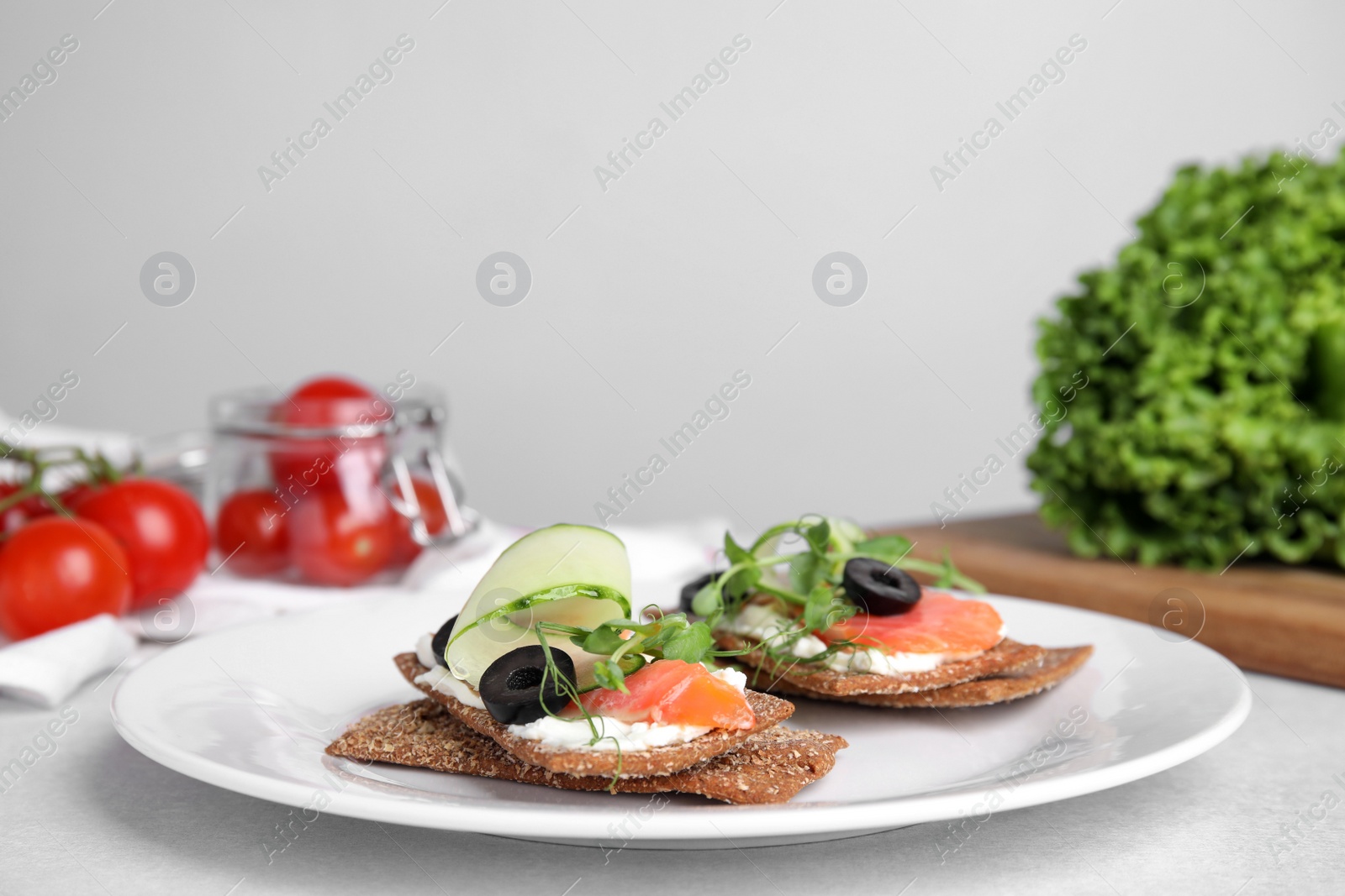 Photo of Tasty rye crispbreads with salmon, cream cheese and vegetables served on light grey table