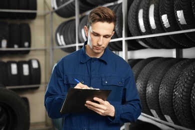 Young male mechanic with clipboard near tires in automobile service center