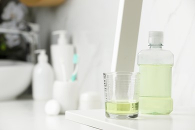 Photo of Bottle of mouthwash and glass on white shelf in bathroom, space for text