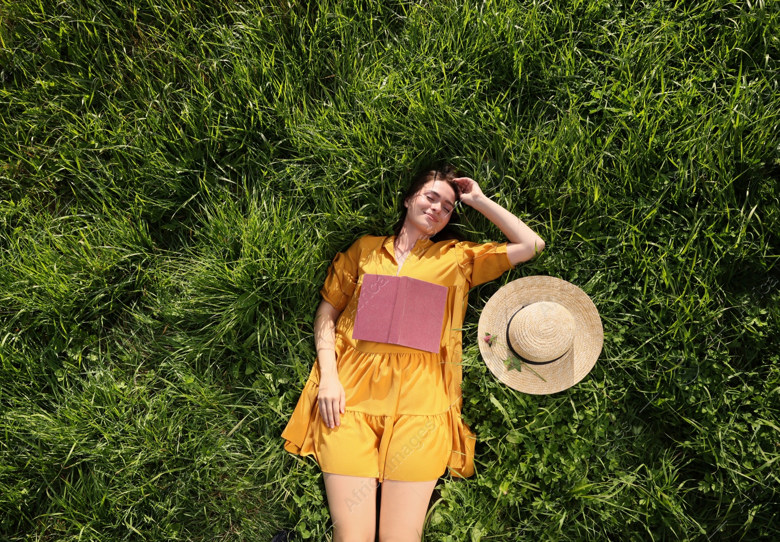 Photo of Beautiful young woman with book lying on green meadow, top view. Summer reading