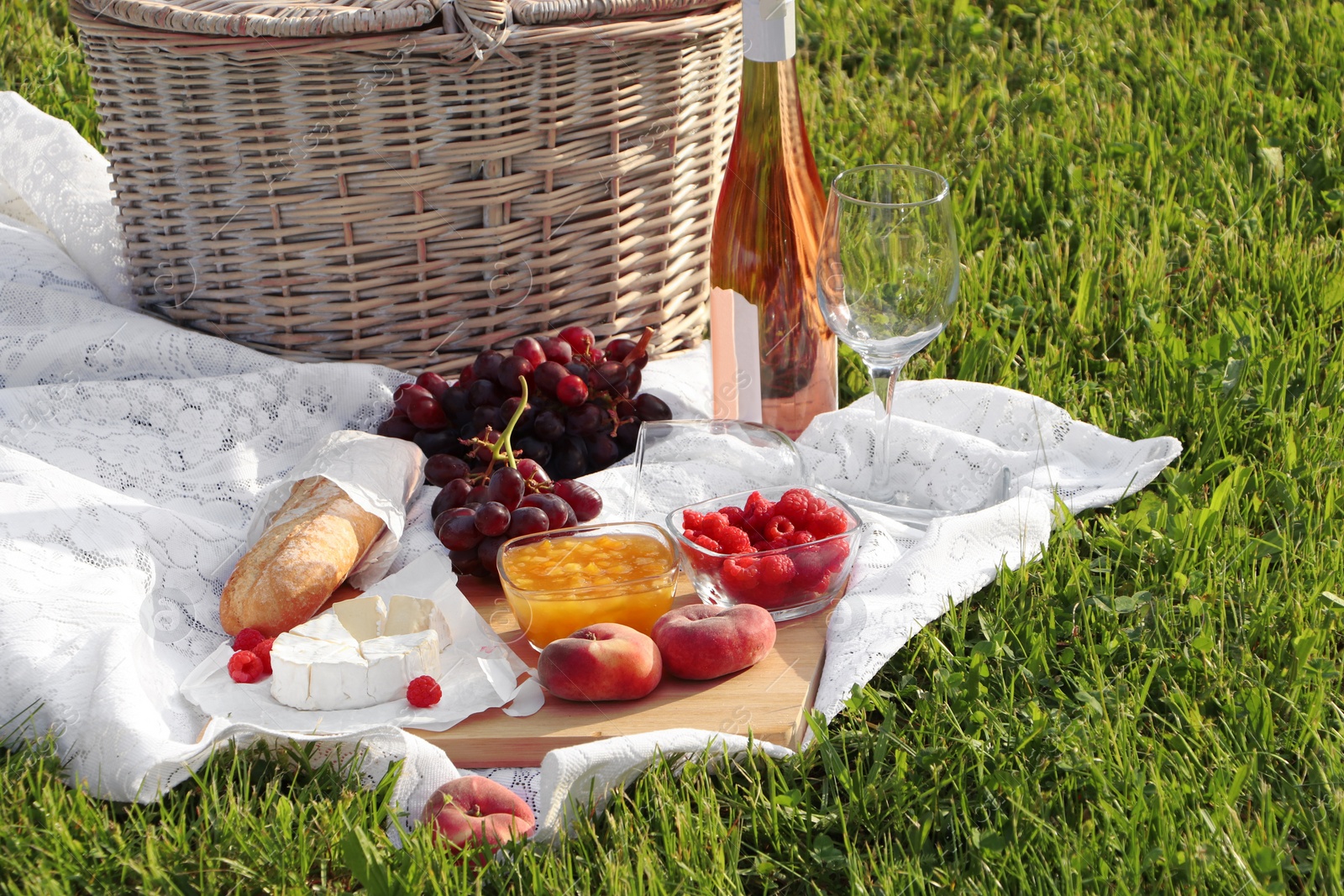 Photo of Picnic blanket with tasty food, basket and cider on green grass outdoors