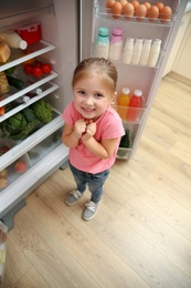 Photo of Cute little girl feeling cold near open refrigerator at home