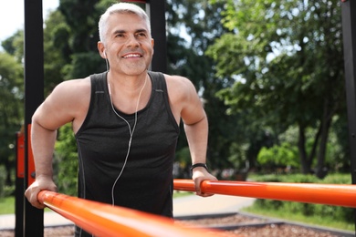 Handsome mature man doing exercise on sports ground, space for text. Healthy lifestyle