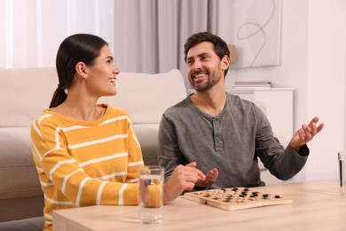 Happy couple talking while playing checkers at wooden table in room