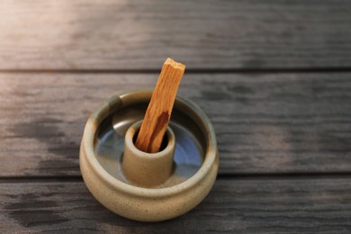 Palo santo stick in holder on wooden table, closeup