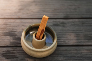 Photo of Palo santo stick in holder on wooden table, closeup