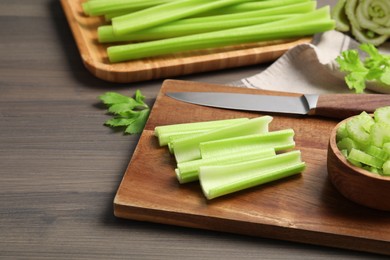 Photo of Board with fresh green cut celery and knife on wooden table, space for text
