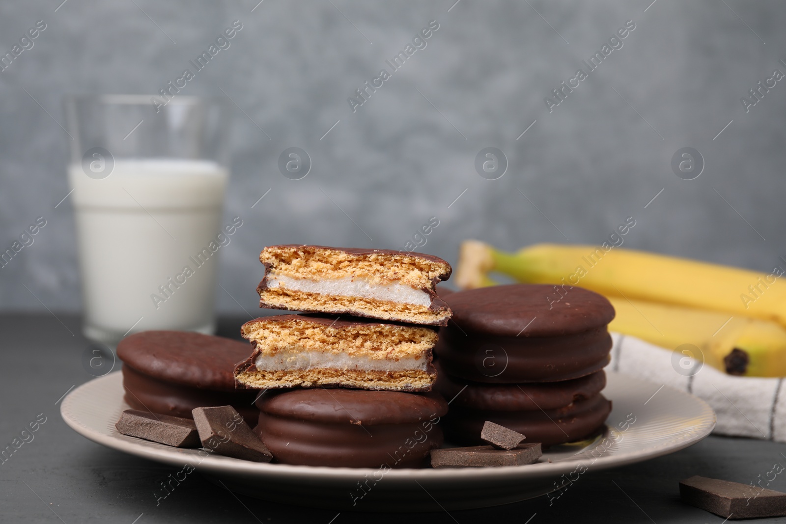 Photo of Plate with tasty banana choco pies and pieces of chocolate on grey table, closeup. Space for text