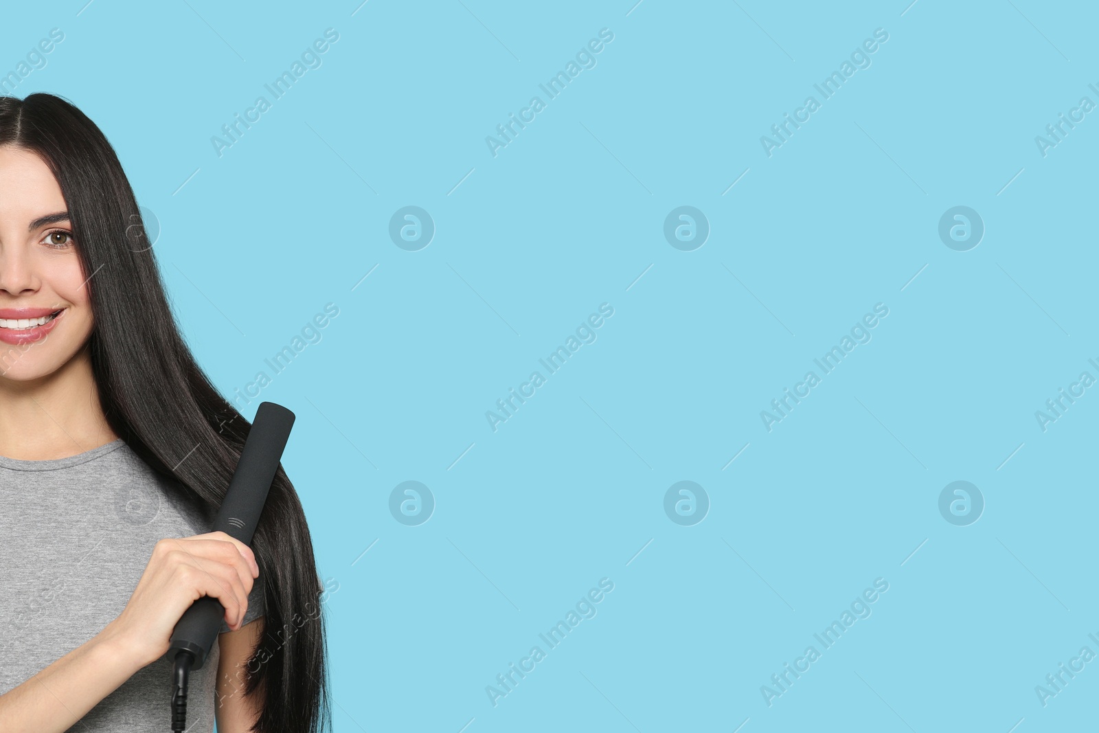 Photo of Beautiful happy woman using hair iron on light blue background, closeup. Space for text