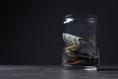 Photo of Donation jar with money on table against dark background. Space for text