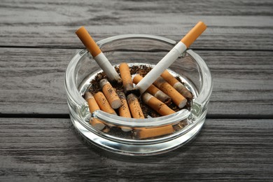 Photo of Glass ashtray with cigarette stubs on black wooden table