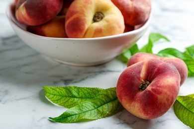 Photo of Fresh ripe donut peaches with leaves on white marble table, closeup