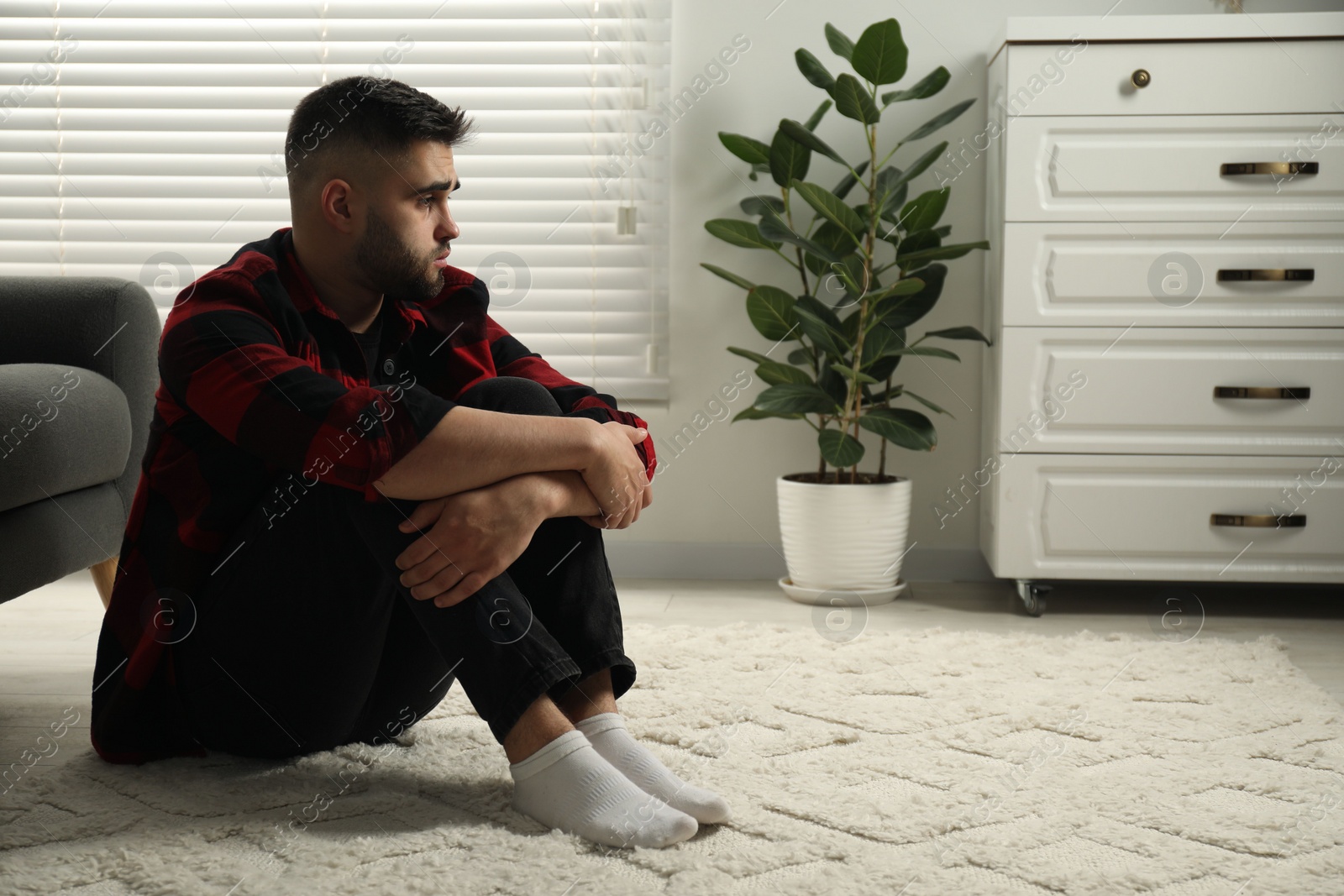 Photo of Sad man sitting on floor at home. Space for text