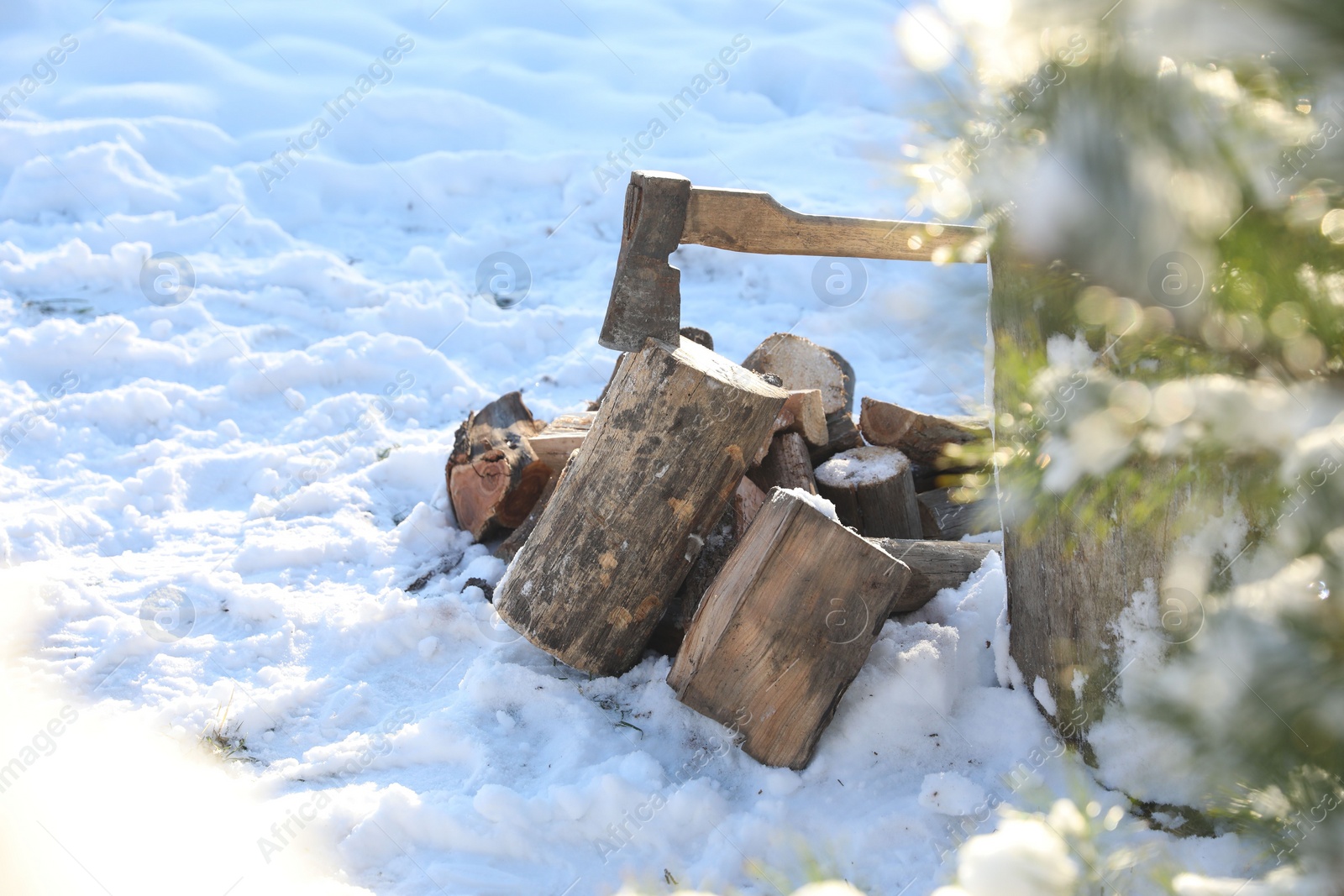 Photo of Metal axe in wooden log and pile of wood outdoors on sunny winter day. Space for text