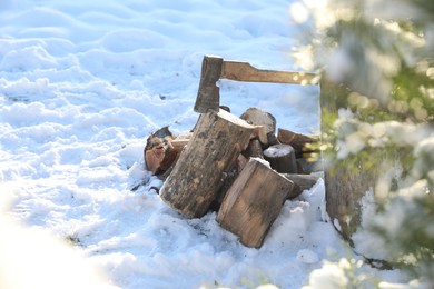 Metal axe in wooden log and pile of wood outdoors on sunny winter day. Space for text