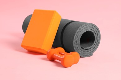 Photo of Grey exercise mat, yoga block and dumbbells on pink background