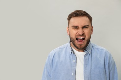 Photo of Angry young man on grey background, space for text. Hate concept