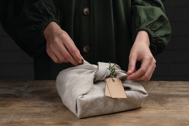 Photo of Furoshiki technique. Woman wrapping gift in fabric at wooden table, closeup