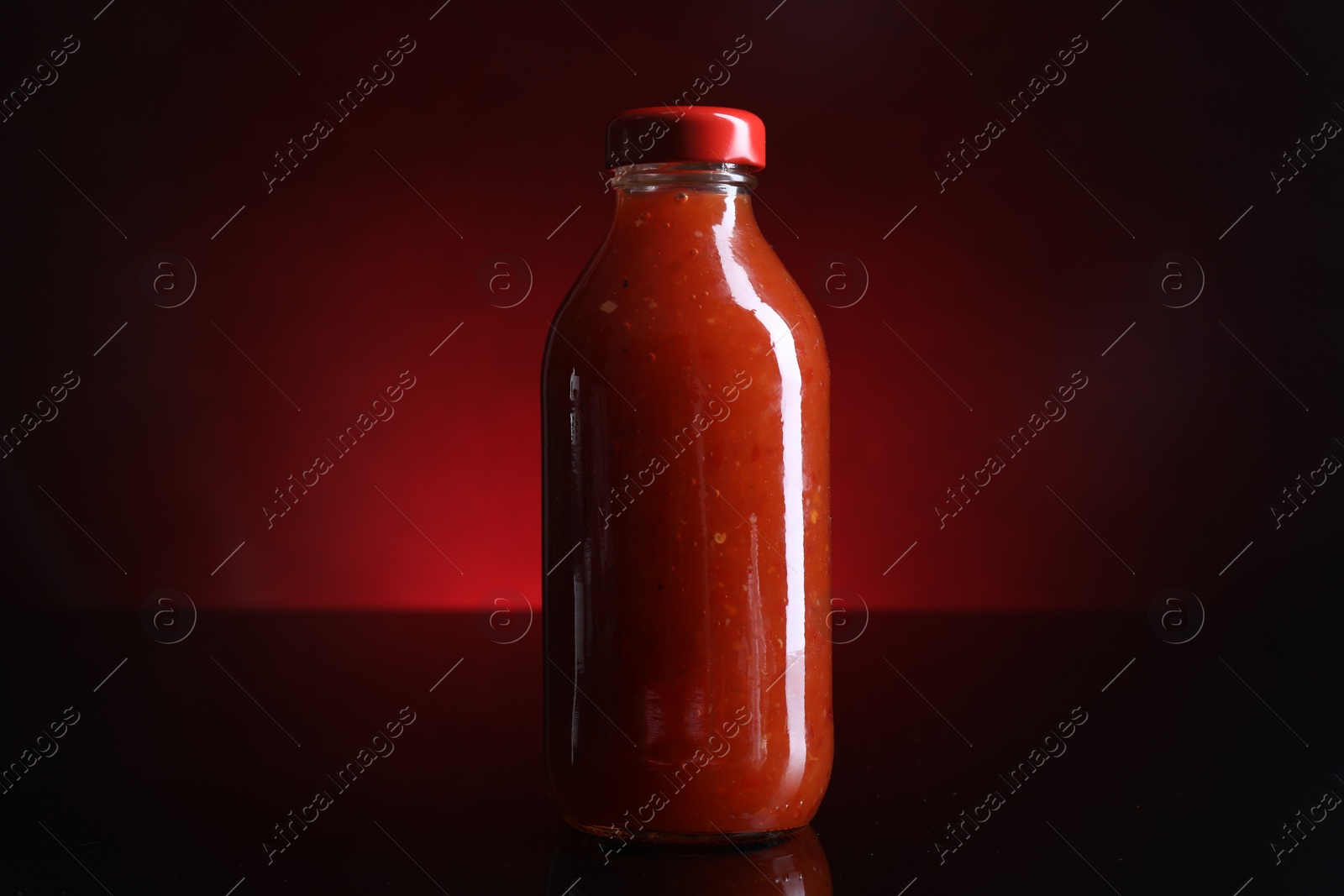 Photo of Spicy chili sauce in bottle on against dark background