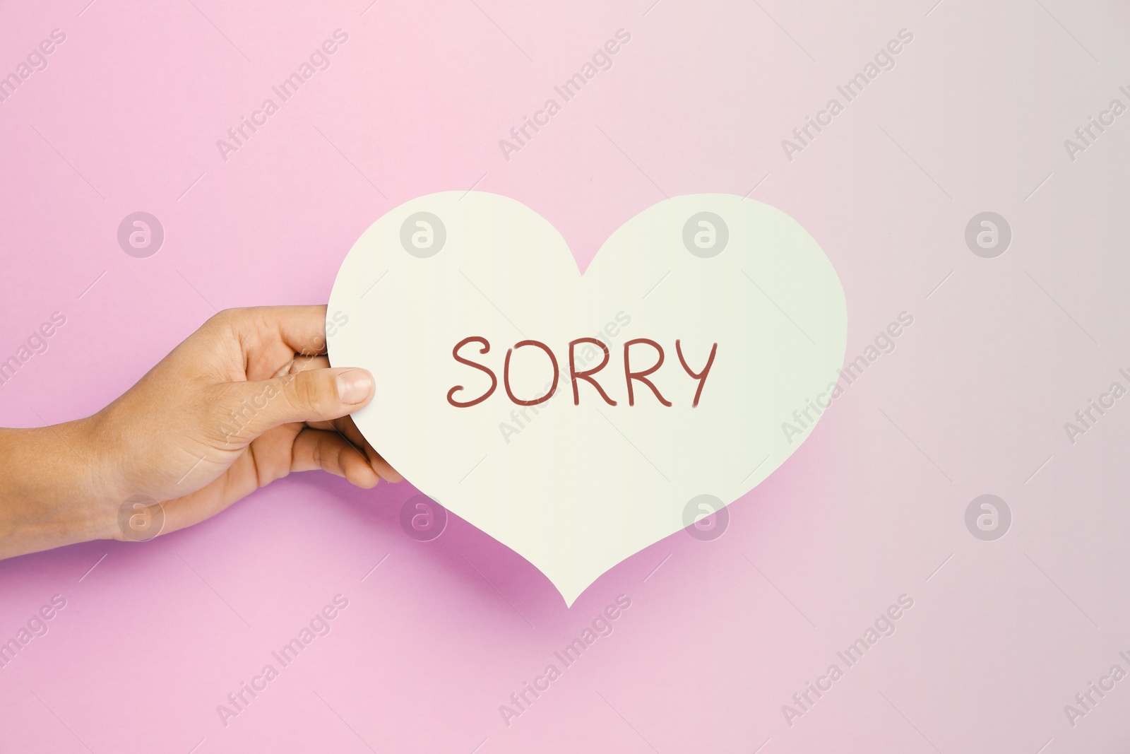 Image of Apology. Woman holding paper heart with word Sorry on pink background, closeup
