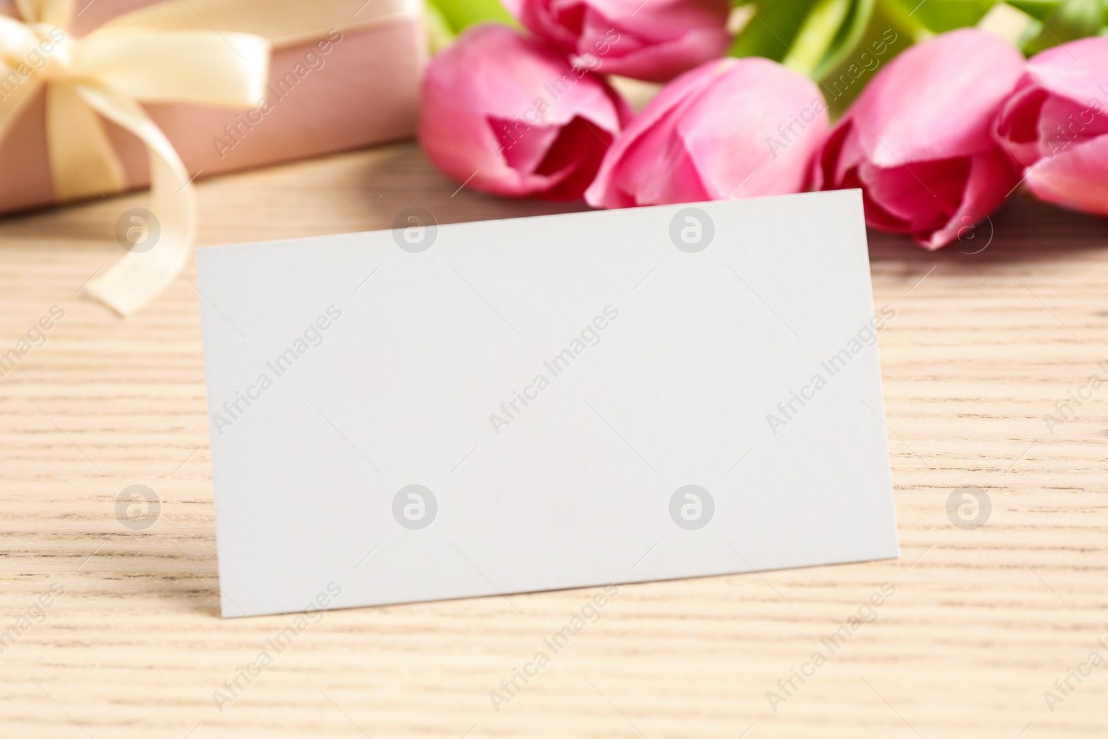 Photo of Greeting card, gift and tulips on wooden table, space for text. Happy Mother's Day