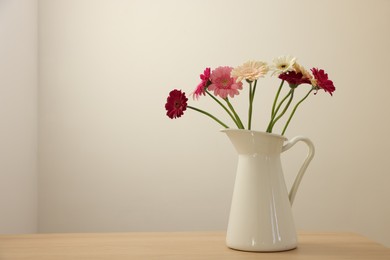 Photo of Jug with beautiful gerbera flowers on wooden table. Space for text