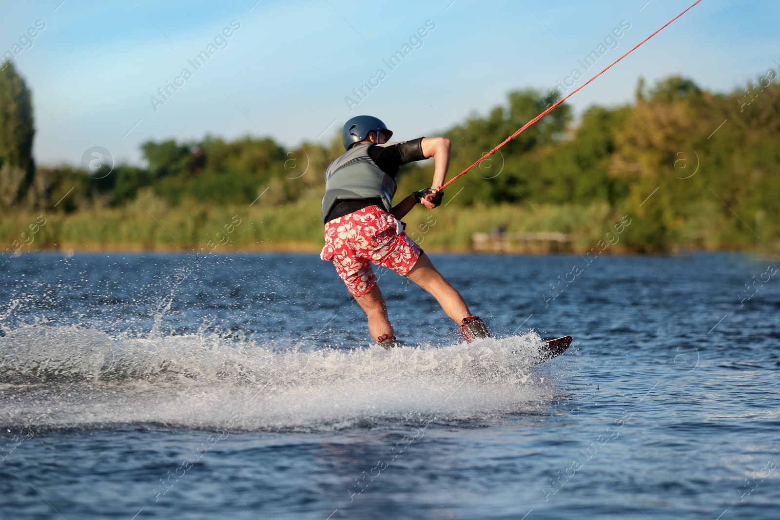 Photo of Teenage boy wakeboarding on river, back view. Extreme water sport